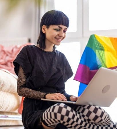 Smiling nonbinary person using a laptop.