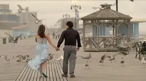 [COURTESY OF KEEP THE CHANGE] - image shows the two lead actors from behind as they walk down the boardwalk holding hands.