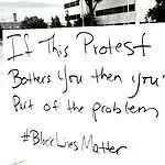 Image description: image is a white cardboard protest sign with the words written in black ink, "If this protest bothers you then you're part of the problem #BlackLivesMatter"