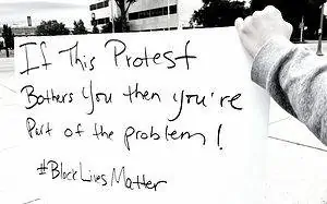 Image description: image is a white cardboard protest sign with the words written in black ink, "If this protest bothers you then you're part of the problem #BlackLivesMatter"