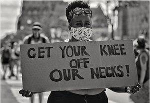 Black woman at a protest in a facemask holding a sign Get Your Knee Off Our Necks