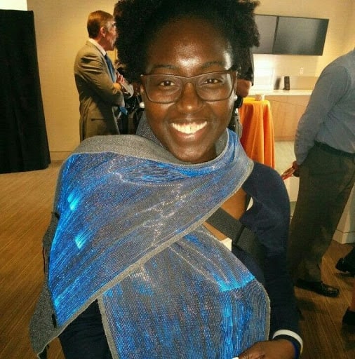 DeVan L. Hankerson, African-American woman with deep-brown skin and natural hair. She is wearing dark brown-rimmed glasses and looking directly into the camera with a big, dazzling smile. She is wearing pearl earrings and she has an electric blue scarf around her neck. She is also wearing a black blazer and she has white nail-polish on her fingers.