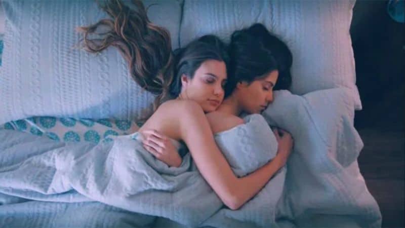 Two Mexican Latina women with long brunette hair in bed cuddling