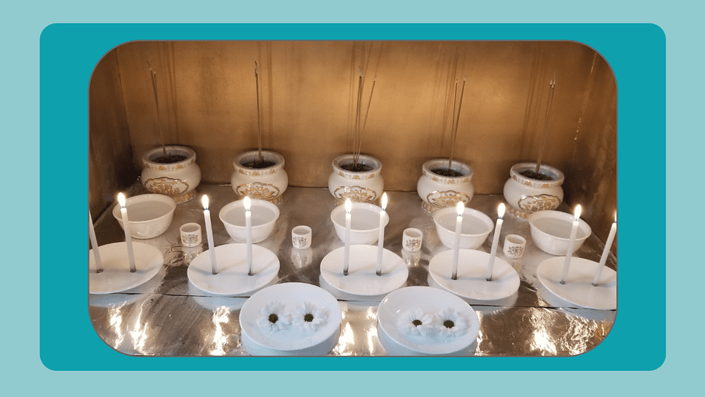 A teal and light teal background with a photo in the middle. The photo is of Nancy's Hmong shaman altar. There are white and gold bowls with incense in them, white bowls and cups with water in them, white plates with candles on them, and two plates with white daisies on them.