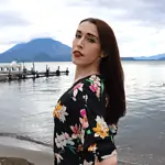 Latina trans woman with red lipstick and long brown hair in floral black dress in front of Lake Atitlan in Guatemala