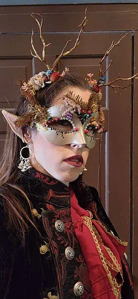 Kayley Whalen wearing elf ears and a carnival mask and antlers with mushroom earrings and a Renaissance style shirt.