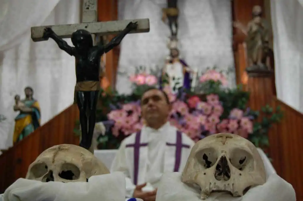 A church in  San José Guatemala with a priest leading a ceremony with skulls on the altar as part of the annual "procession of the skulls" ritual.