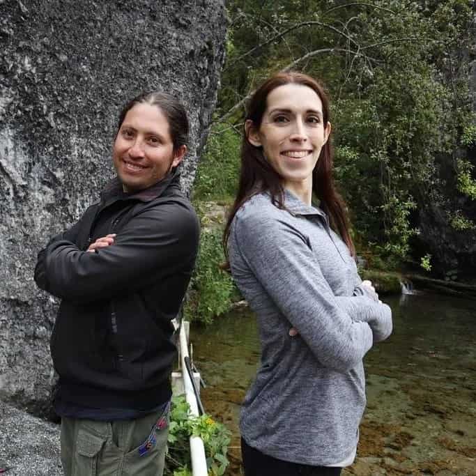 Kayley Whalen with a local Guatemalan tour guide in Los Cuchumatanes mountains with a cliff face and pond behind them. They are standing back-to-back and smiling.