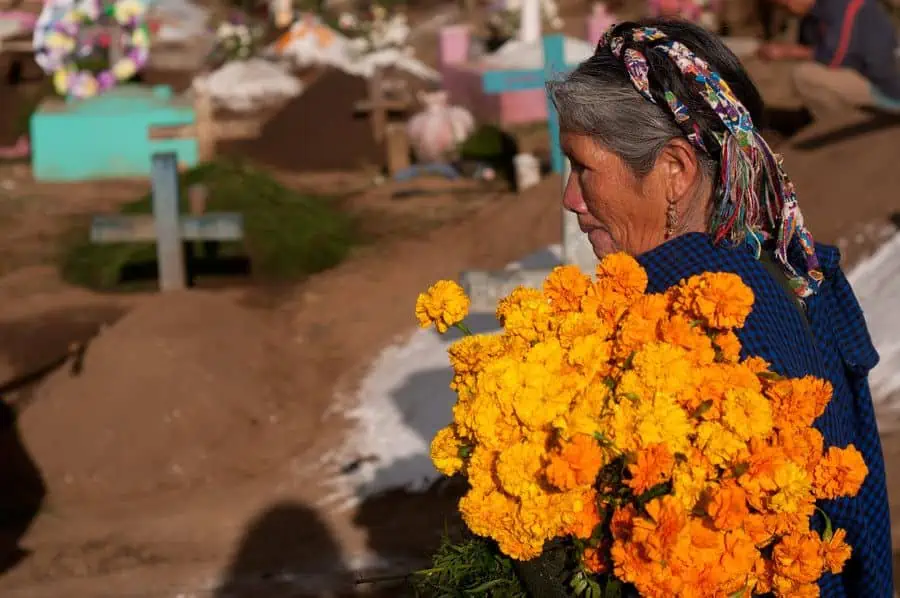 Elderly Guatemalan woman wearing traditional Maya headdress carrying marigolds (Flowers of the Dead) to a grave.