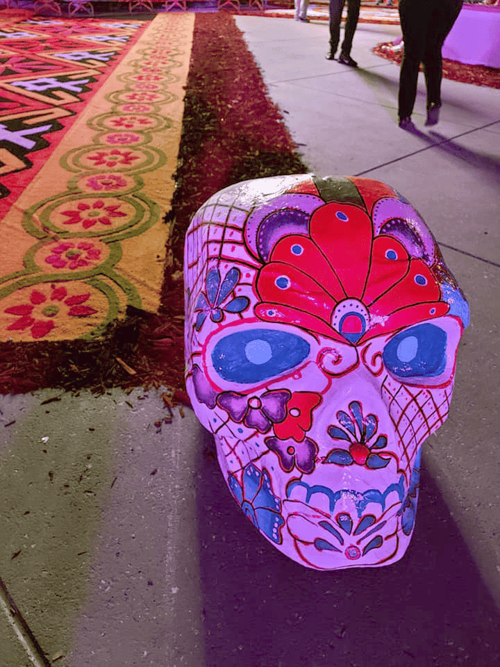 Large sugar skull decoration in Mexico City Day of the Dead celebration in 2021. Visible in the background is colorful patterns made out of painted sand.